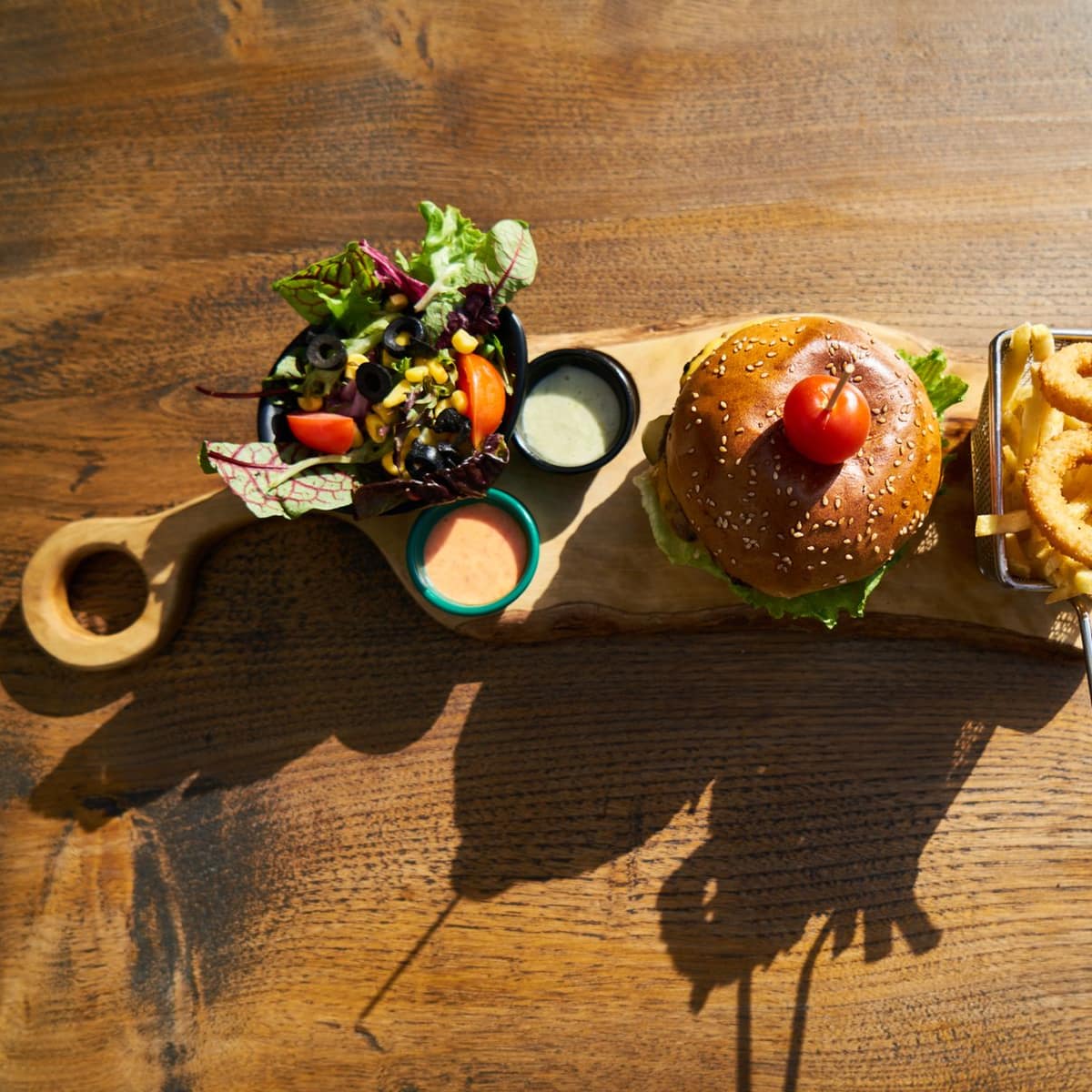 Loaded burger with fries and onion rings on a board